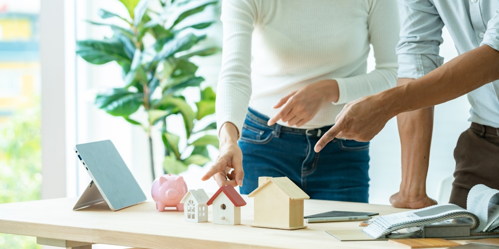 Couple thinking and pointing at three different pretend houses.